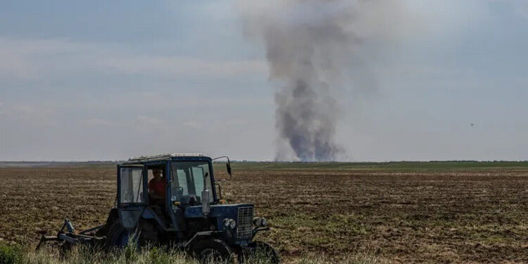 Seorang petani mengoperasikan traktor di wilayah Kherson saat asap mengepul di kejauhan setelah serangan militer Rusia. Foto: Al Jazeera