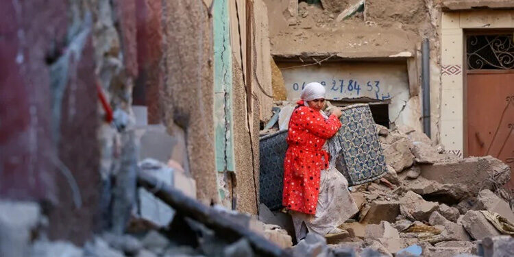 Seorang wanita membawa barang-barangnya keluar dari gedung yang rusak pasca gempa mematikan di Moulay Brahim, Maroko. Foto: Al Jazeera